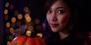 一个穿着女巫服装的亚洲女人拿着一个橙色的南瓜。年轻女性参加了万圣节派对。朋友们在万圣节派对上玩得很开心。