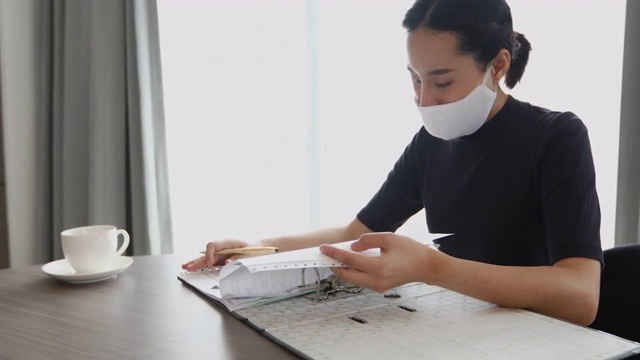 亚洲女性拿着文件，签署工作文件，在办公室戴着口罩