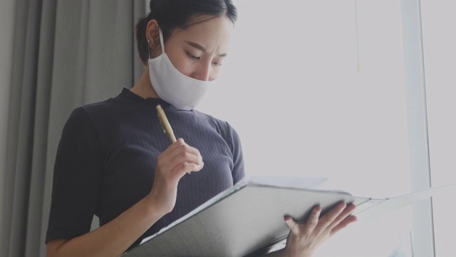 亚洲女性拿着文件，审查工作文件，在办公室戴着口罩