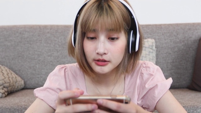 亚洲女性喜欢在家里放松的时候戴着耳机在手机上听音乐