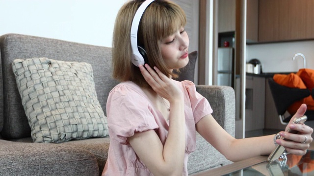 亚洲女性喜欢在家里放松的时候戴着耳机在手机上听音乐