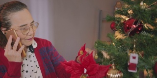 亚洲老女人喜欢在家里装饰圣诞树和打电话。
