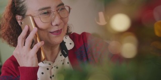 亚洲老女人喜欢在家里装饰圣诞树和打电话。