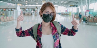一幅亚洲妇女戴着口罩，竖起大拇指，邀请你在机场旅行的肖像