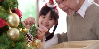 快乐的亚洲女孩和她的祖父几世同堂装饰圣诞树一起准备快乐的节日冬天。