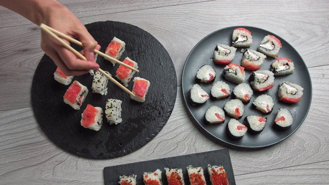 女人用筷子拿食物。日本食品成分。各种寿司摆放在黑石板上。辣泡菜沙拉，馄饨汤，筷子和酱油碗