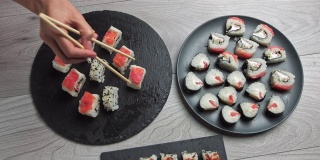 女人用筷子拿食物。日本食品成分。各种寿司摆放在黑石板上。辣泡菜沙拉，馄饨汤，筷子和酱油碗