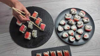 女人用筷子拿食物。日本食品成分。各种寿司摆放在黑石板上。辣泡菜沙拉，馄饨汤，筷子和酱油碗视频素材模板下载