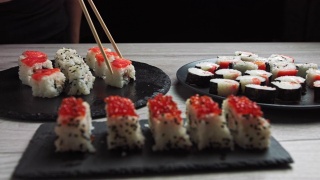 寿司卷与金枪鱼，鲑鱼，黄瓜，鳄梨撒芝麻种子在黑色背景特写。餐厅里各式各样的日本料理视频素材模板下载