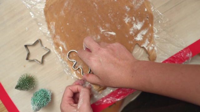 正上方，视角:亚洲妇女的手准备装饰自制圣诞饼干，星星，姜饼在木制的圣诞桌子上装饰小圣诞树由压紧的金属模具淀粉。
