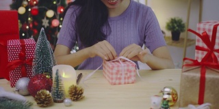 亚洲妇女打开礼盒与笑脸在家里的背景与圣诞树装饰节日节日。圣诞节庆祝活动的概念。4 k慢动作。