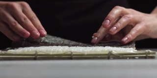 寿司厨师将日本寿司饭铺在紫菜上，做成美味的寿司卷。-高角度拍摄