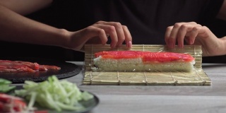 日本厨师准备用三文鱼和鳄梨做寿司卷。厨师双手在竹席上制作日本寿司卷。美味的日本料理，低角度视野