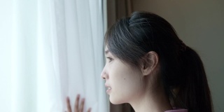 一个年轻的亚洲女人在早上透过窗户看风景的场景