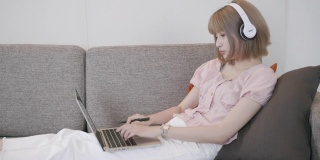 一个亚洲女人坐在沙发上，用笔记本电脑在家里学习电子学习