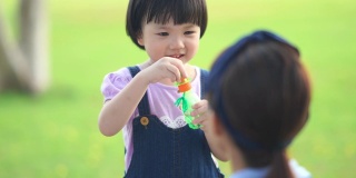 亚洲女孩在花园里和妈妈玩泡泡，学龄前