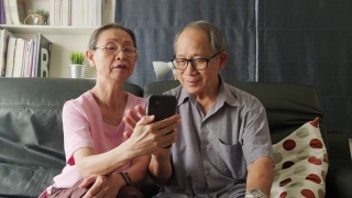 亚洲老年妇女和老人手持手机或平板电脑，在家里与儿子、女儿、孙子、孙女进行视频通话和微笑。祖父母对通过互联网交流感到高兴。视频素材模板下载