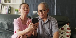亚洲老年妇女和老人手持手机或平板电脑，在家里与儿子、女儿、孙子、孙女进行视频通话和微笑。祖父母对通过互联网交流感到高兴。