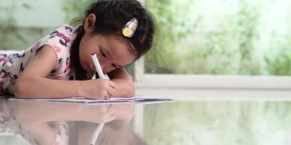 小孩子学生或小女孩喜欢写作，在家里的白纸上画颜料。幸福家庭与儿童发展理念。