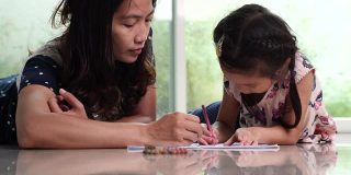 Young mom and little cute daughter enjoy drawing coloring picture with pencils. Happy Family and Children Development Concept.