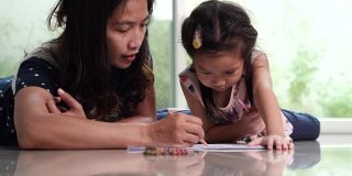 年轻的妈妈和可爱的女儿喜欢用铅笔画彩色图画。幸福家庭与儿童发展理念。