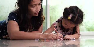 年轻的妈妈和可爱的女儿喜欢用铅笔画彩色图画。幸福家庭与儿童发展理念。