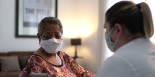医生在老年妇女病人家中与她交谈-使用口罩