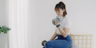 亚洲女强人在家用哑铃锻炼。居家隔离预防冠状病毒和新冠病毒感染的运动概念。4 k慢动作。