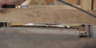 一个木材工匠正在用一个手持电动饰面板切割一块旧胡桃木板。