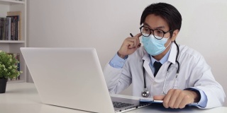 亚洲医生戴眼镜和口罩通过视频电话建议和检查患者