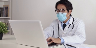 亚洲医生在办公室使用笔记本电脑时戴上眼镜和口罩