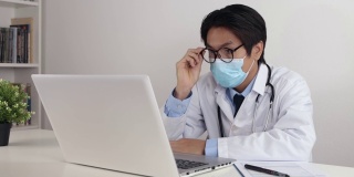 亚洲医生戴口罩戴眼镜在办公室使用笔记本电脑