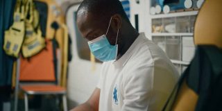 疲惫的非洲裔美国医护人员戴着口罩，试图在一辆前往紧急情况的救护车上休息。紧急医疗技术人员正在前往医疗保健医院外的途中。