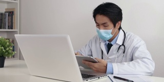 亚洲医生戴口罩检查身体检查报告从平板在办公室