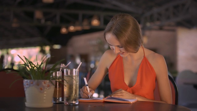 女人在桌上用果汁微笑，翻着日记
