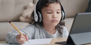 教育。亚洲小女孩做作业用平板电脑和耳机在早上。在家在线学习的概念