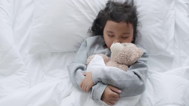 一个亚洲小女孩在卧室里睡觉，抱着泰迪熊