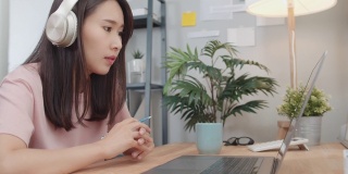 亚洲女商人戴着耳机用笔记本电脑与同事进行视频通话，并在网上讨论商业项目。