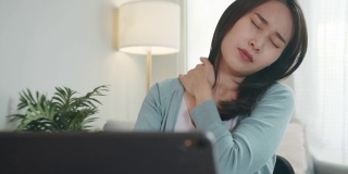 疲惫美丽的亚洲女商人坐在办公桌前感到疲惫，颈部疼痛，肩膀触摸，自我按摩，伸展疼痛的脸。办公室综合症的概念。