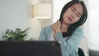 疲惫美丽的亚洲女商人坐在办公桌前感到疲惫，颈部疼痛，肩膀触摸，自我按摩，伸展疼痛的脸。办公室综合症的概念。视频素材模板下载