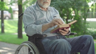 无法辨认的瘫痪老人翻动书页，大声朗读。白发苍苍的退休白人在阳光明媚的夏日公园里享受文学。爱好和残疾。视频素材模板下载