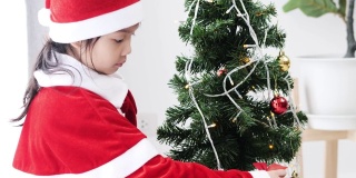 亚洲女孩穿着圣诞老人的服装，在家里装饰圣诞树，生活理念。