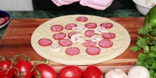 一位戴着粉色手套的厨师将蘑菇片放在准备好的披萨面团上。在家做披萨