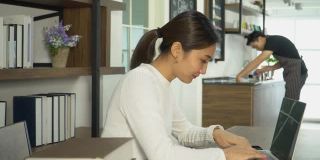 迷人的亚洲年轻女子在咖啡馆用笔记本电脑工作。