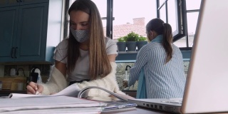 COVID-19大流行期间的在家教育。一个年轻的青少年和一个私人教师戴着防护口罩，在家庭气氛中上课。记笔记。平曲线。