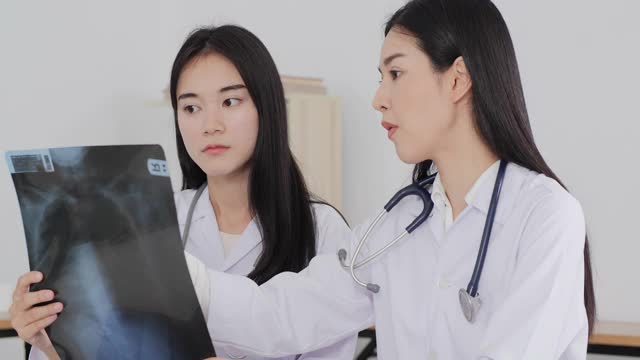 两名身穿实验室大褂的亚洲妇女在医院工作，其中一名妇女拿着一张x光片，正在和另一名妇女交谈。