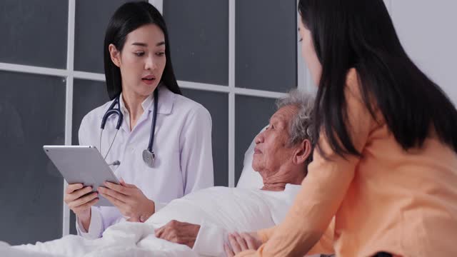 亚洲女医生与一个躺在床上的老病人女人谈话，亚洲女医生谁使用数字平板电脑工作。