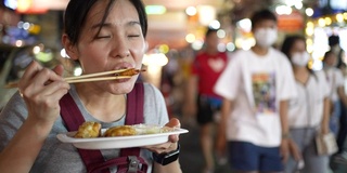 年轻的亚洲女人在街上吃街头小吃