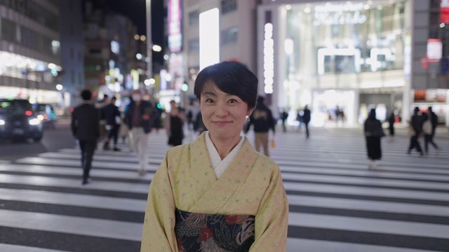 身着和服的日本妇女站在夜间城市的斑马线上