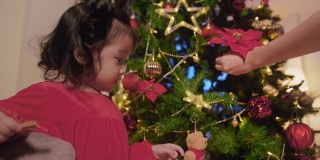 亚洲小女孩喜欢在家里装饰圣诞树。可爱的小女儿玩她的十二月假期。